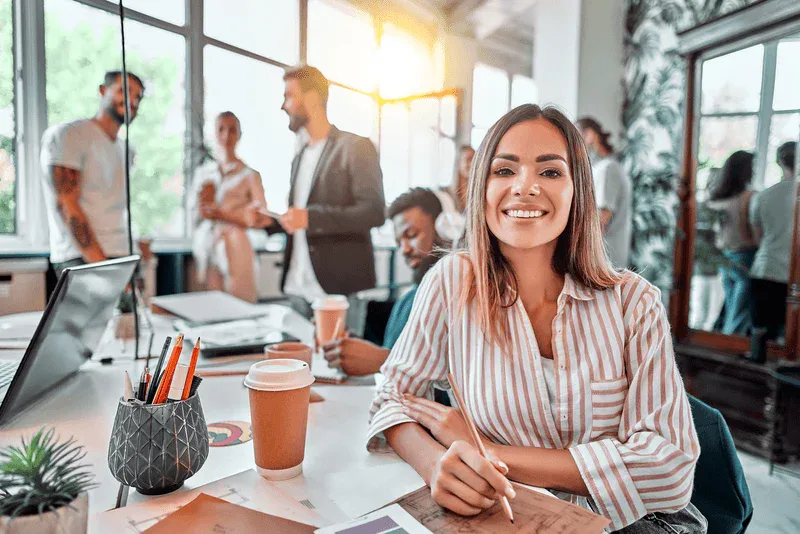 A woman is smiling while sitting at a desk in an office, featuring Data Field Technology Services and highlighting their expertise in innovative tech solutions.